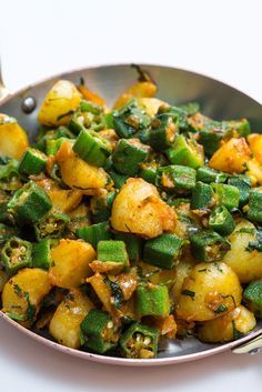 a pan filled with potatoes and green peppers on top of a table next to a fork