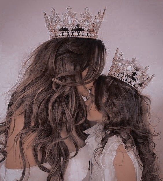 two women wearing tiaras kissing each other in front of a white wall with long hair