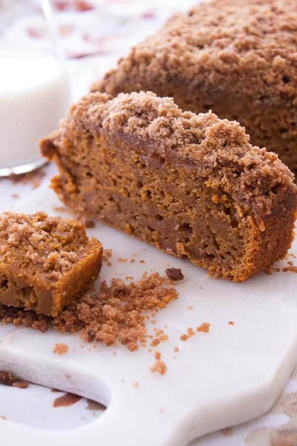 pumpkin loaf cake with streusel topping is cut into slices and sits on a white plate