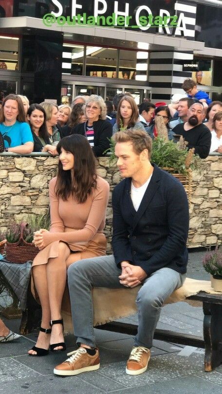 two people sitting on a bench in front of a group of people with plants behind them