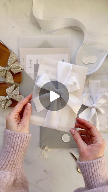 two hands holding a white card with bows on it and another person's shoes next to it