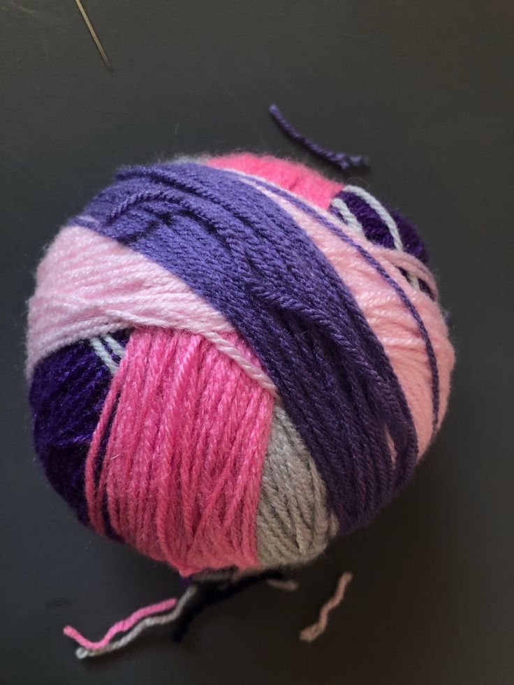 a ball of yarn with pink, purple and white stripes on it next to a pair of scissors