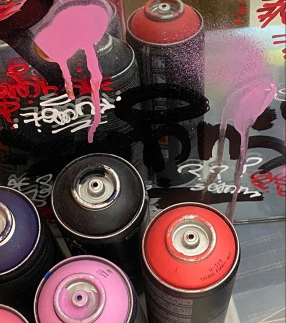 several cans of spray paint sitting in front of a store display window with graffiti on it