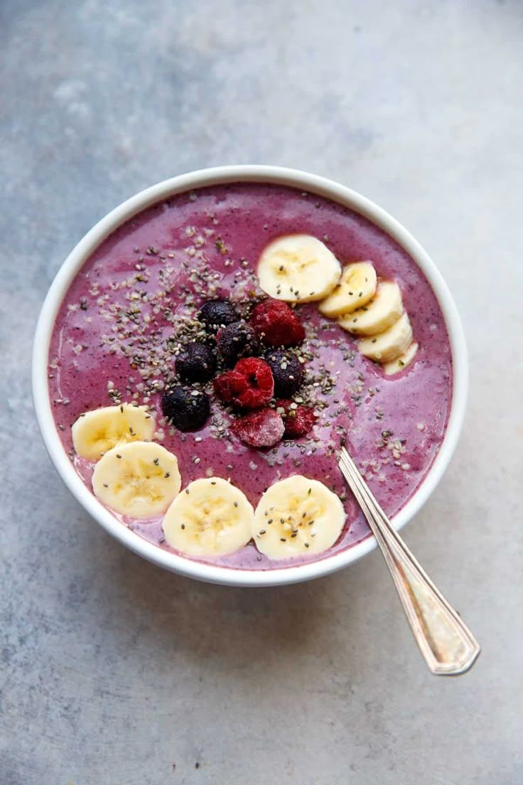 a bowl of smoothie topped with bananas and raspberries next to a spoon