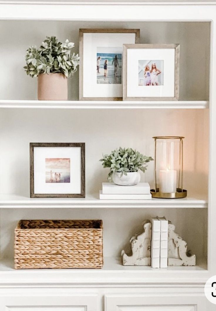 a white book shelf with pictures and plants on it