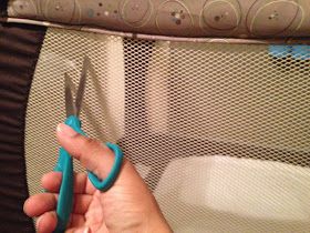 a person holding scissors in their hand near a crib with a mattress behind them