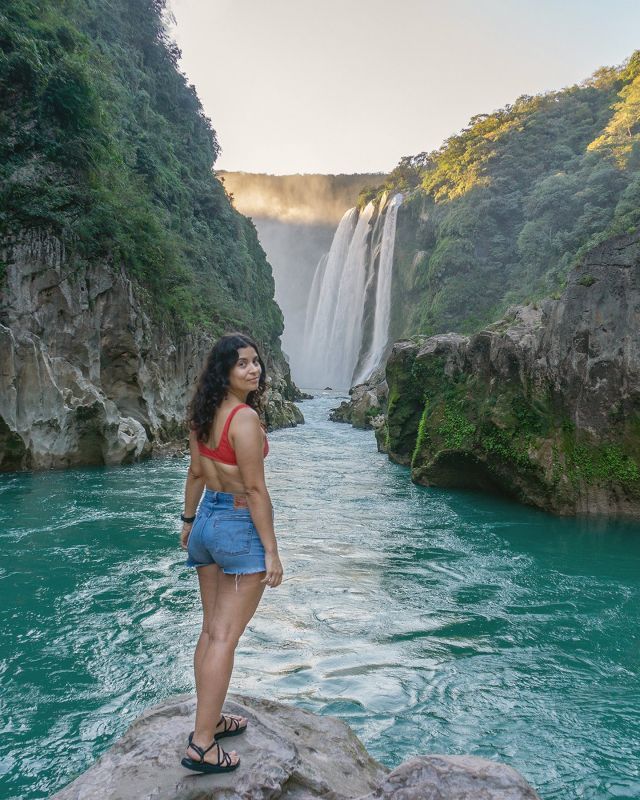 a woman standing on top of a rock in front of a waterfall and blue water