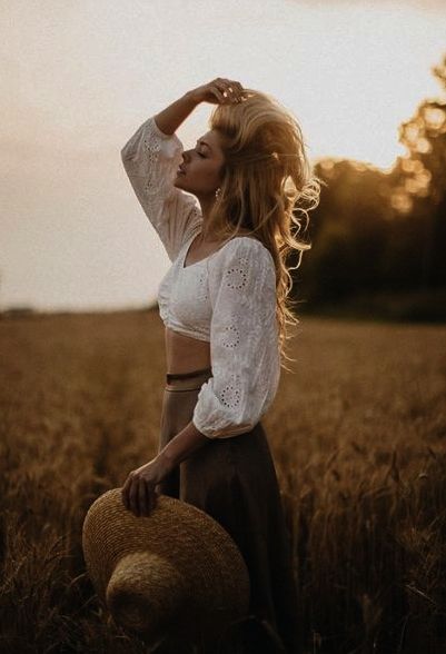 a woman standing in a wheat field with her hands on her head while wearing a hat