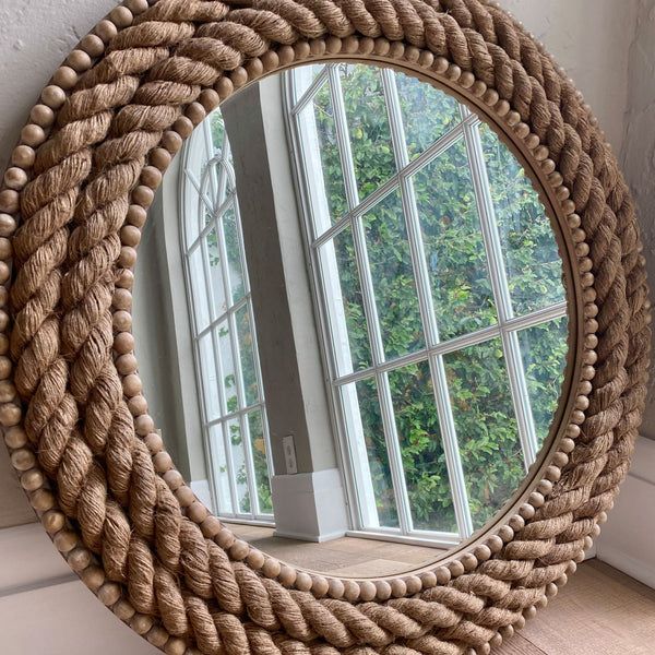 a round rope mirror hanging on the wall next to a window with an open window pane