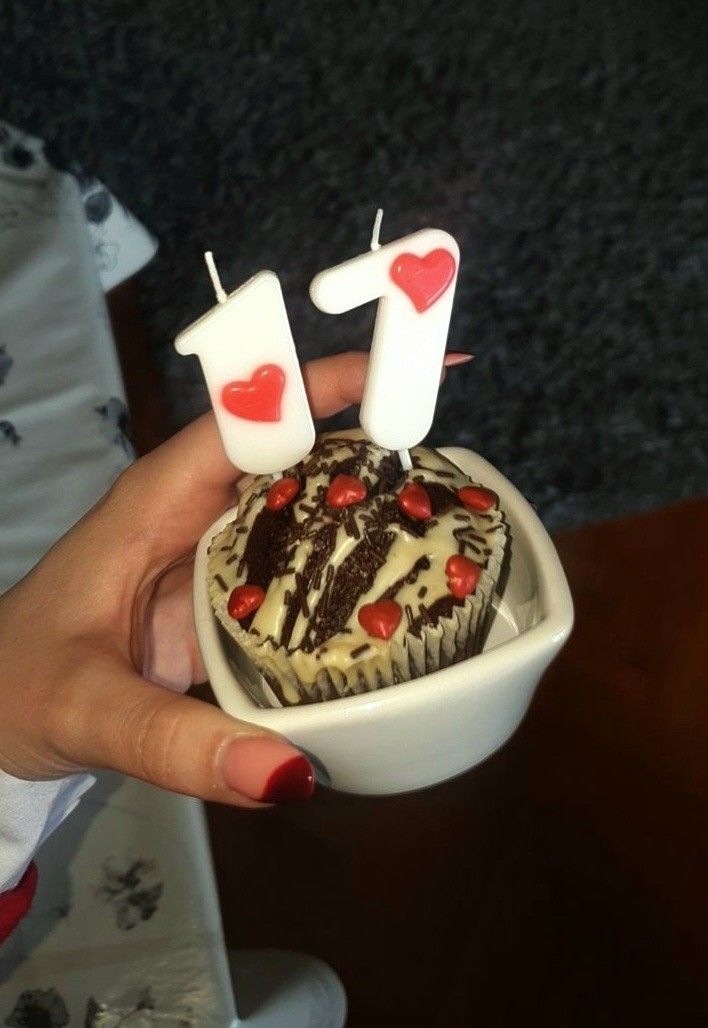 a cupcake with candles in the shape of two hearts is held by a woman's hand