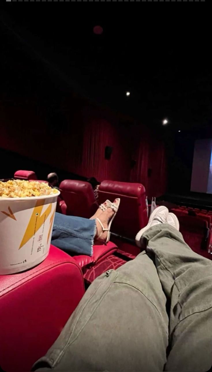 a person laying on the floor in front of a movie theater with their feet up next to a bucket of popcorn