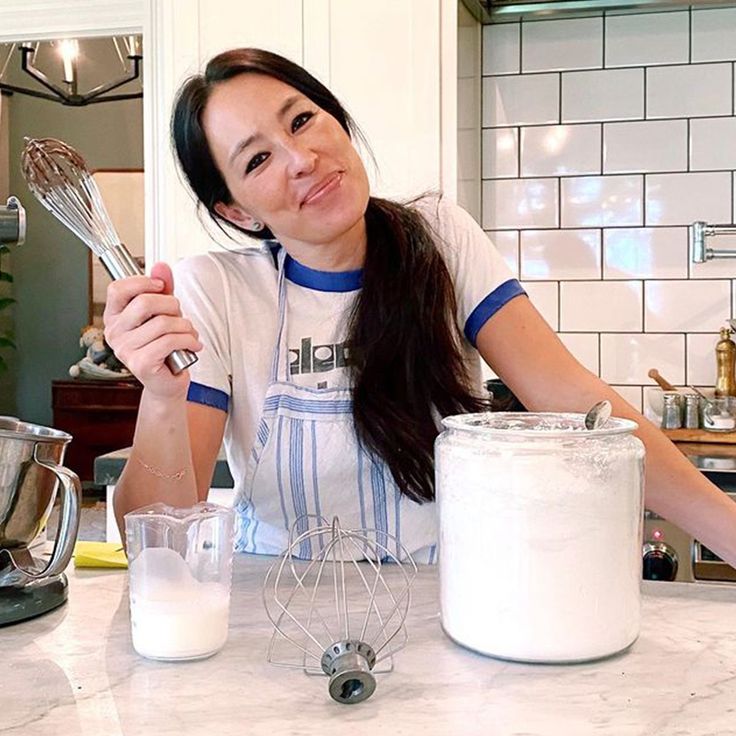 a woman holding a whisk in her right hand while sitting at a kitchen counter