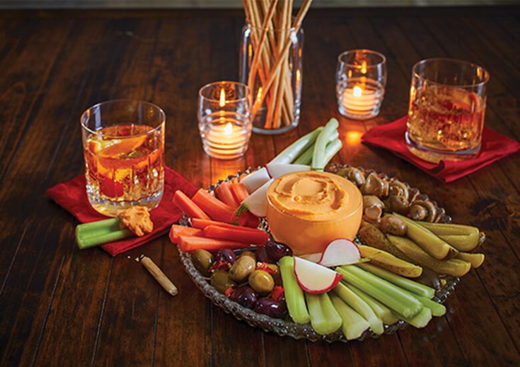 an assortment of fruits and vegetables on a tray next to glasses with candles in them