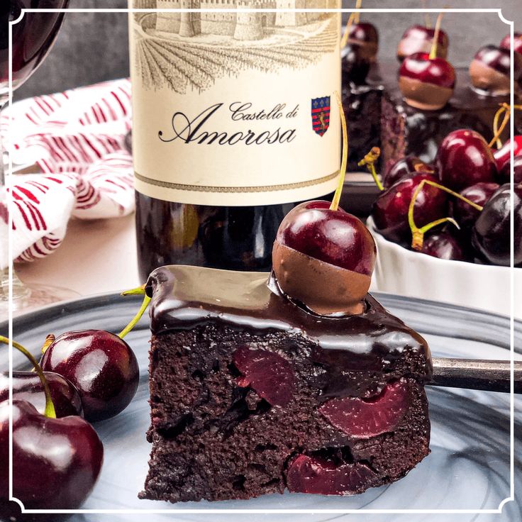 a piece of chocolate cake on a plate with cherries and a bottle of wine in the background