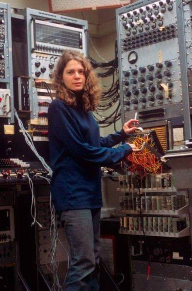 a woman standing in front of an array of electronic equipment with wires running through her hands