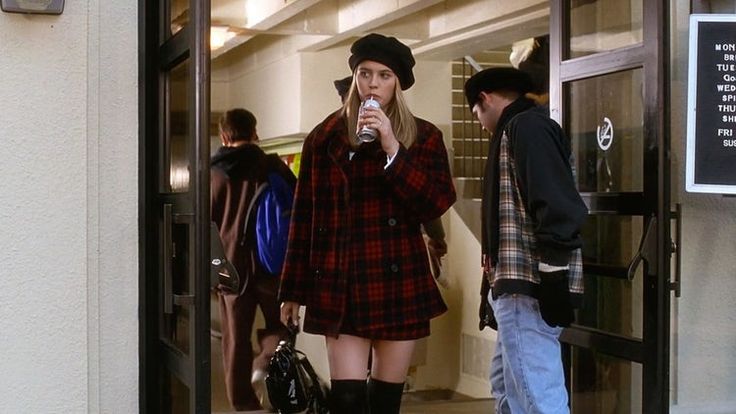 a woman in short shorts and knee high boots is drinking from a cup while another man stands behind her