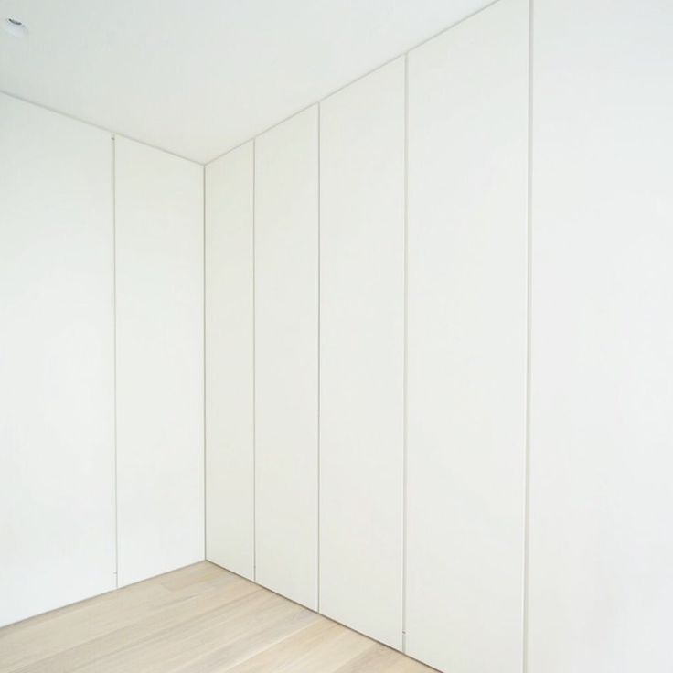 an empty room with white walls and wood flooring is seen in this image from the corner