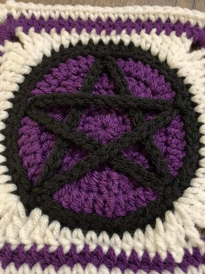 a purple and white crocheted square with black circles on it's center