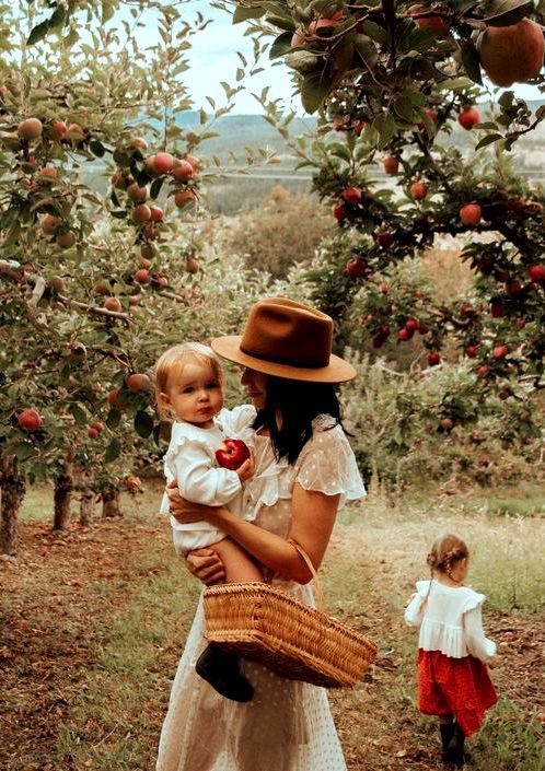 a woman holding a baby in an apple orchard