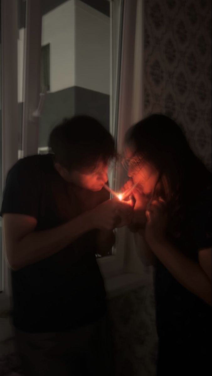 two people standing next to each other in front of a window with the lights on