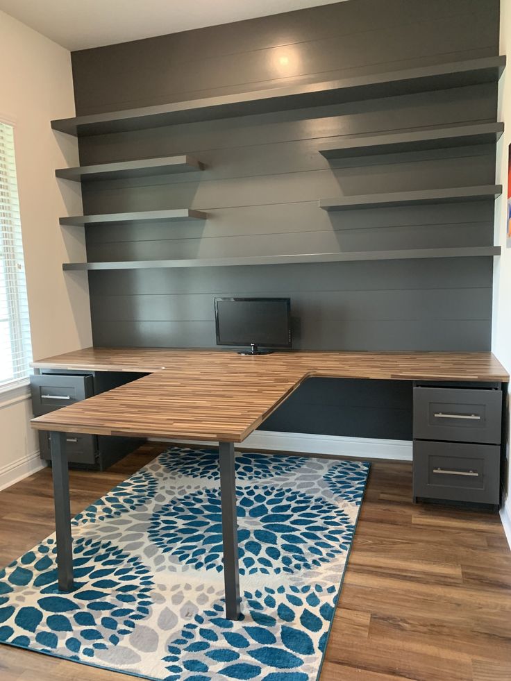 a room with a desk, shelves and rug on the floor in front of it