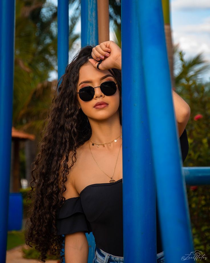 a woman with long hair and sunglasses standing in front of some blue poles holding her head