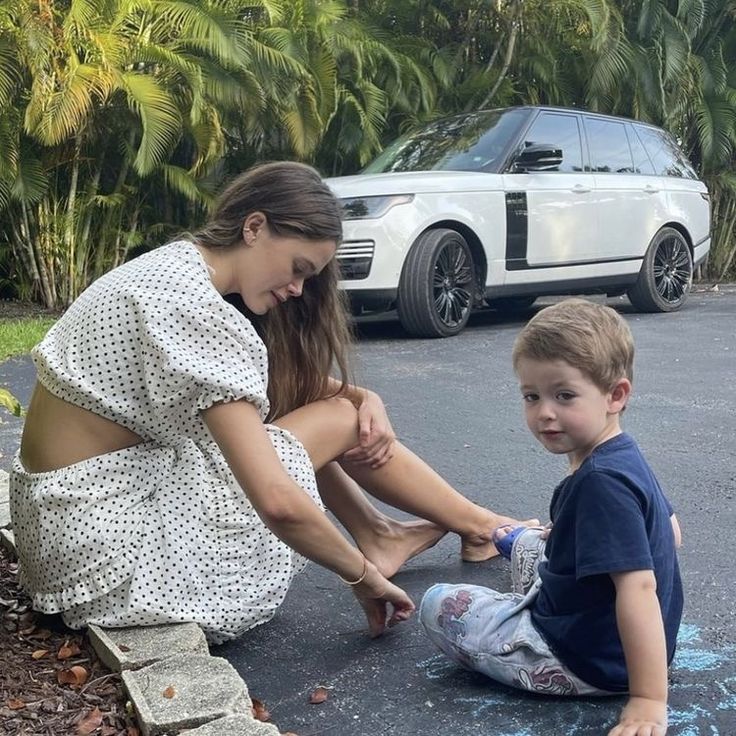 a woman sitting on the ground next to a little boy