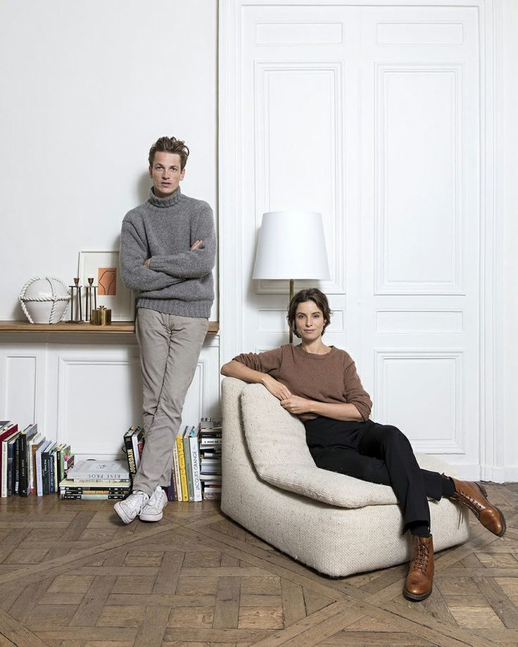 two people sitting on a couch in front of a wall with books and a lamp