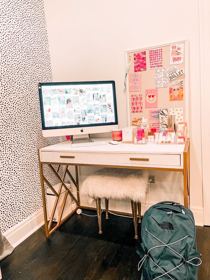 a desk with a computer on it in front of a wallpapered background and a backpack