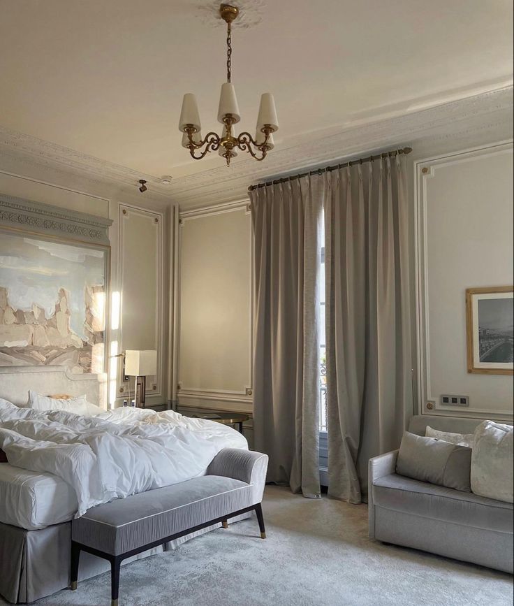 a large white bed sitting in a bedroom next to two chairs and a chandelier