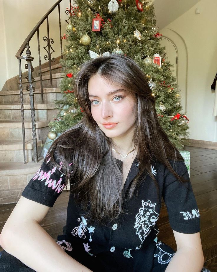 a young woman sitting in front of a christmas tree with her hands on her hips