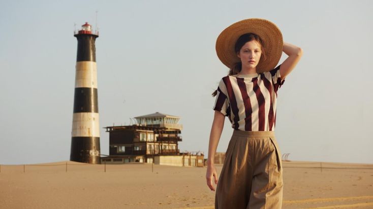 a woman in striped shirt and wide brimmed hat standing next to a light house