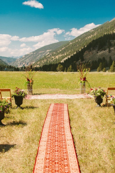 an outdoor ceremony setup with chairs and flowers in vases on the grass, surrounded by mountains