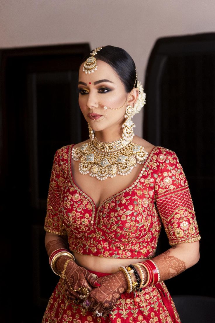 a woman wearing a red and gold bridal outfit with jewelry on her neck, standing in