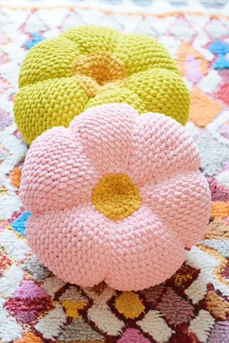 three knitted flower cushions sitting on top of a colorful rug in front of a window