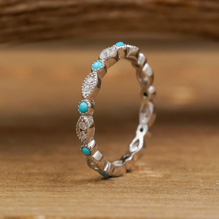 a white gold ring with turquoise stones and diamonds on the inside is sitting on a wooden surface