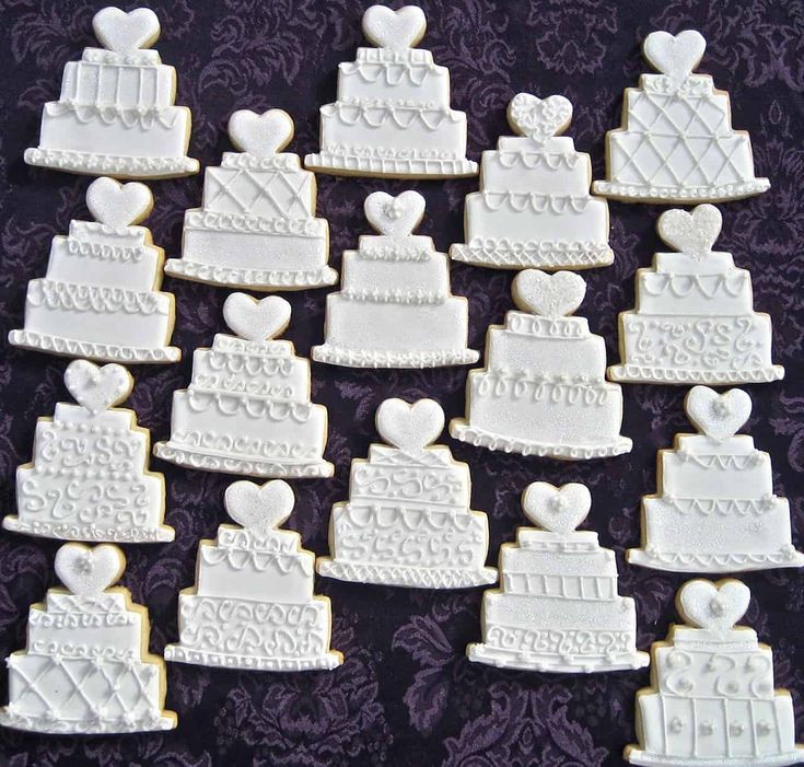 many decorated cookies are arranged in the shape of hearts and wedding cake slices on a purple tablecloth