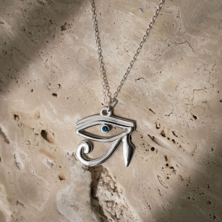 The Eye of Horus necklace is a mystifying piece of jewellery. The necklace features a pendant that is crafted in the shape of the Eye of Horus, an ancient Egyptian symbol of protection, power, and good health.  The pendant is made of sterling silver and has a high polish finish, giving it a luxurious and radiant appearance. At the center of the Eye of Horus pupil is a brilliant 2. 3mm sapphire, which captivatingly brings the piece alive. It is carefully selected for its quality and is set in a s Horus Necklace, Eye Of Horus Necklace, The Eye Of Horus, Ancient Egyptian Symbols, Symbol Of Protection, Egyptian Symbols, August Birthstone Jewelry, July Birthstone Jewelry, Silver Jewelry Necklace