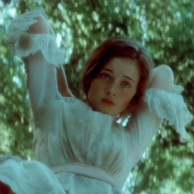 a woman in white dress holding her arms up to the side with trees behind her