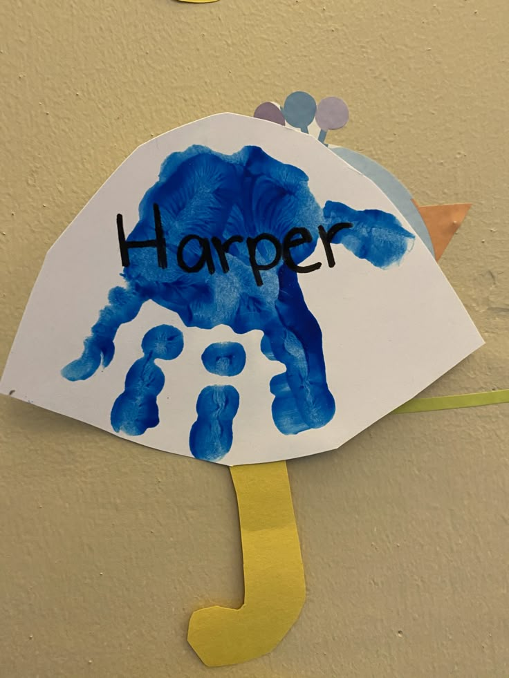 a child's handprinted umbrella hanging on the side of a wall that says harper