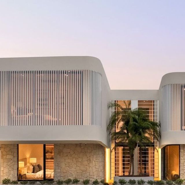 two large white buildings sitting next to each other on the side of a road with palm trees in front of them