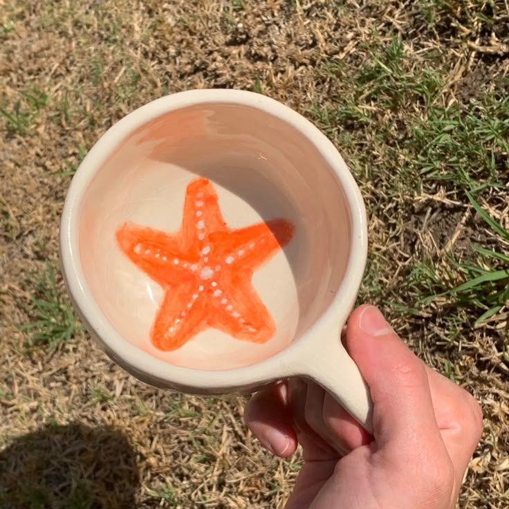 a hand holding a cup with an orange starfish in it