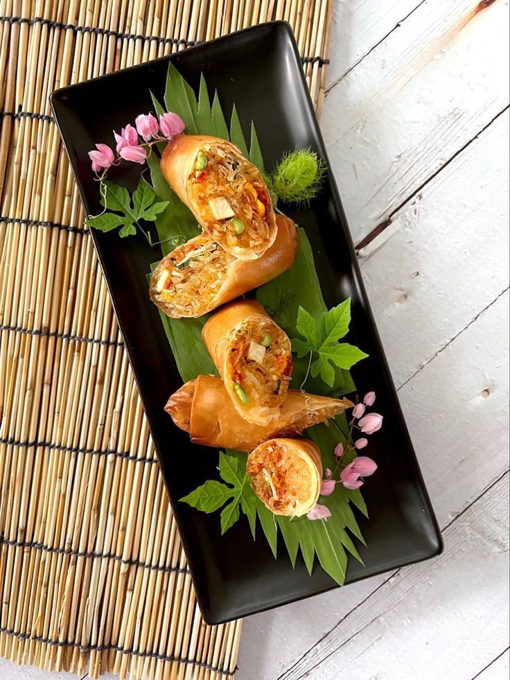 a black plate topped with food on top of a bamboo mat next to a plant