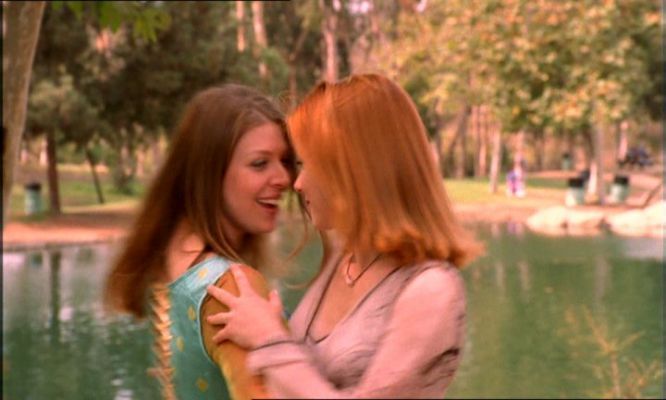 two women standing next to each other in front of a body of water with trees