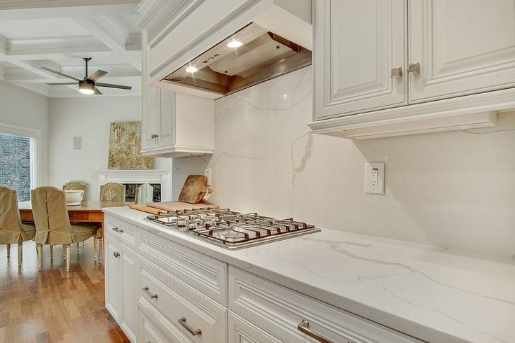 a kitchen with white cabinets and marble counter tops is pictured in this image, there are chairs around the stove