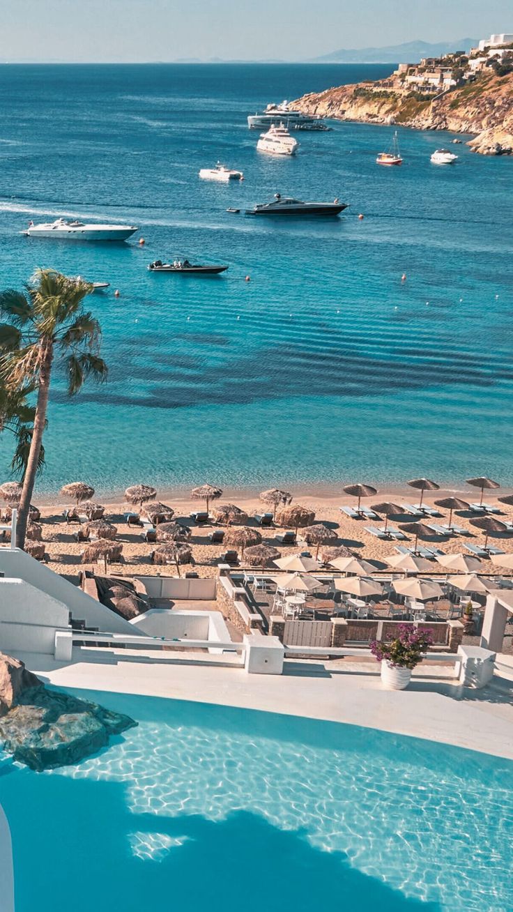 an outdoor swimming pool next to the beach with boats in the water and palm trees