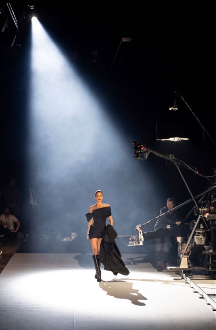 a woman walking down a runway in front of a camera set up for a fashion show