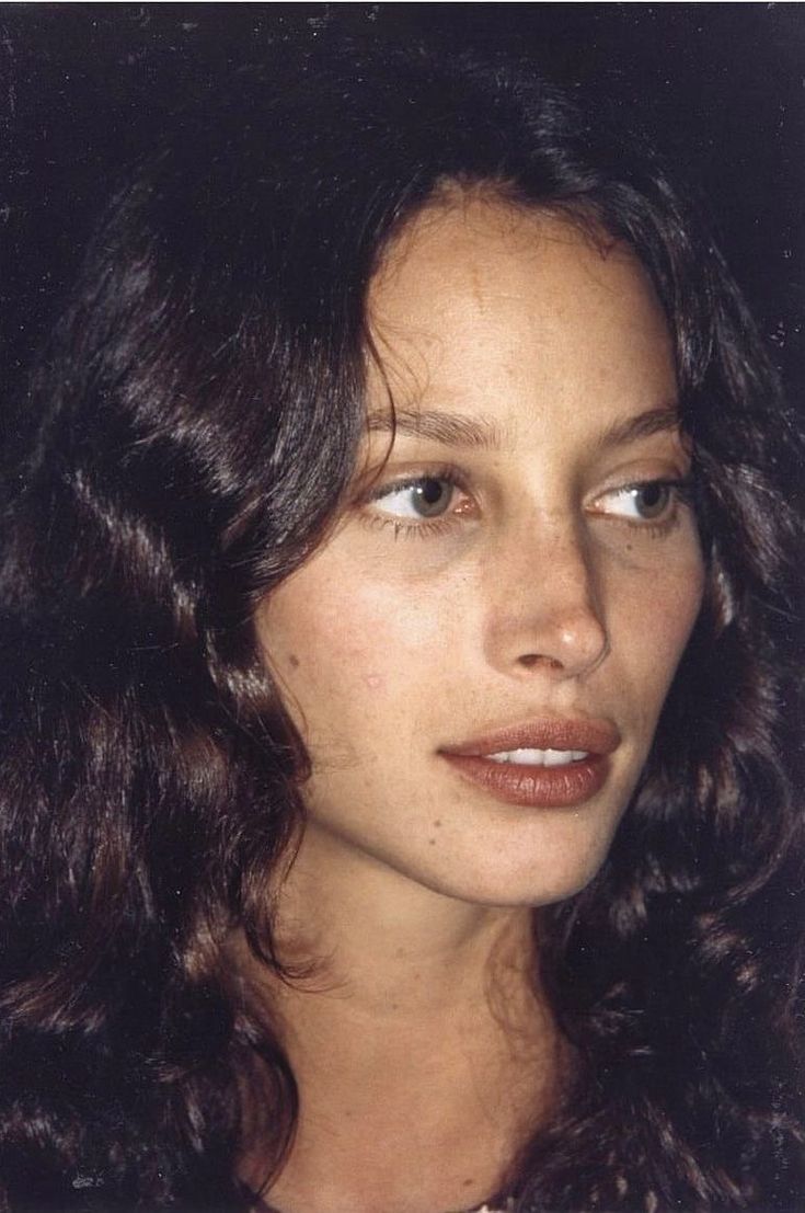 a close up of a woman with dark hair and blue eyes looking at the camera