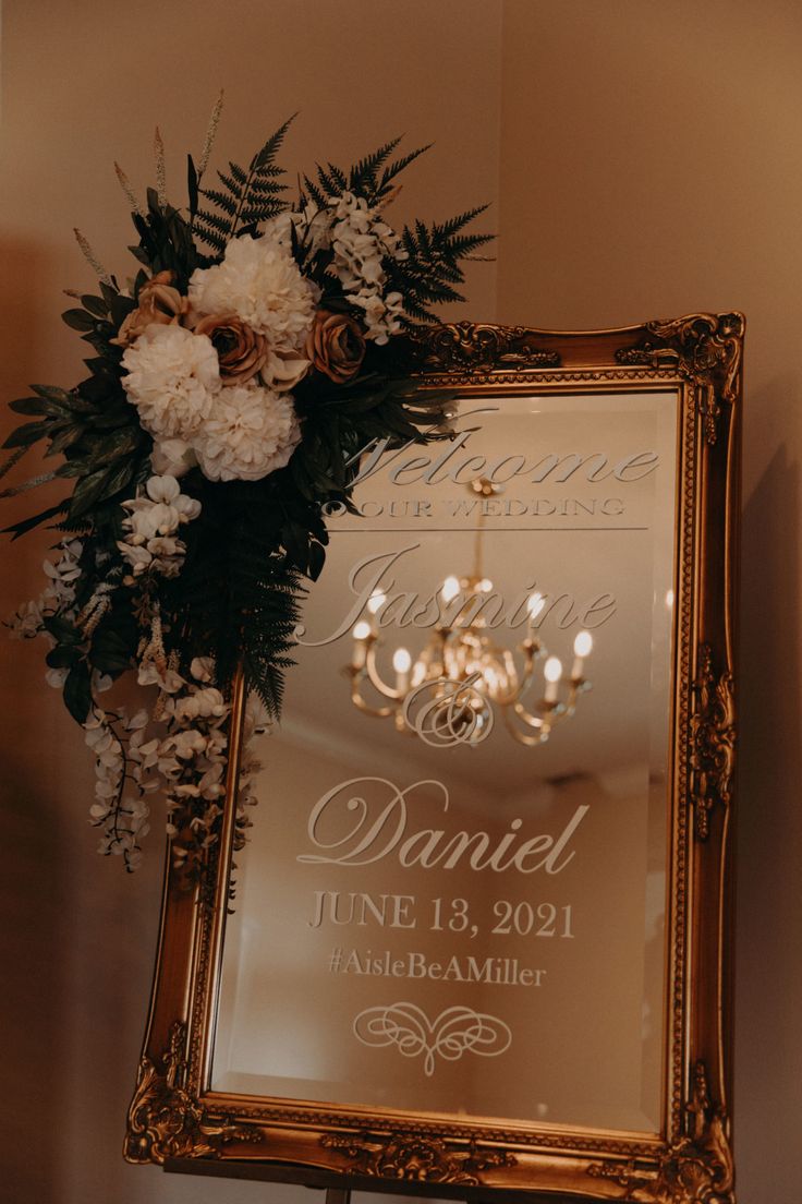 a wedding sign with flowers in front of it and a chandelier hanging from the ceiling