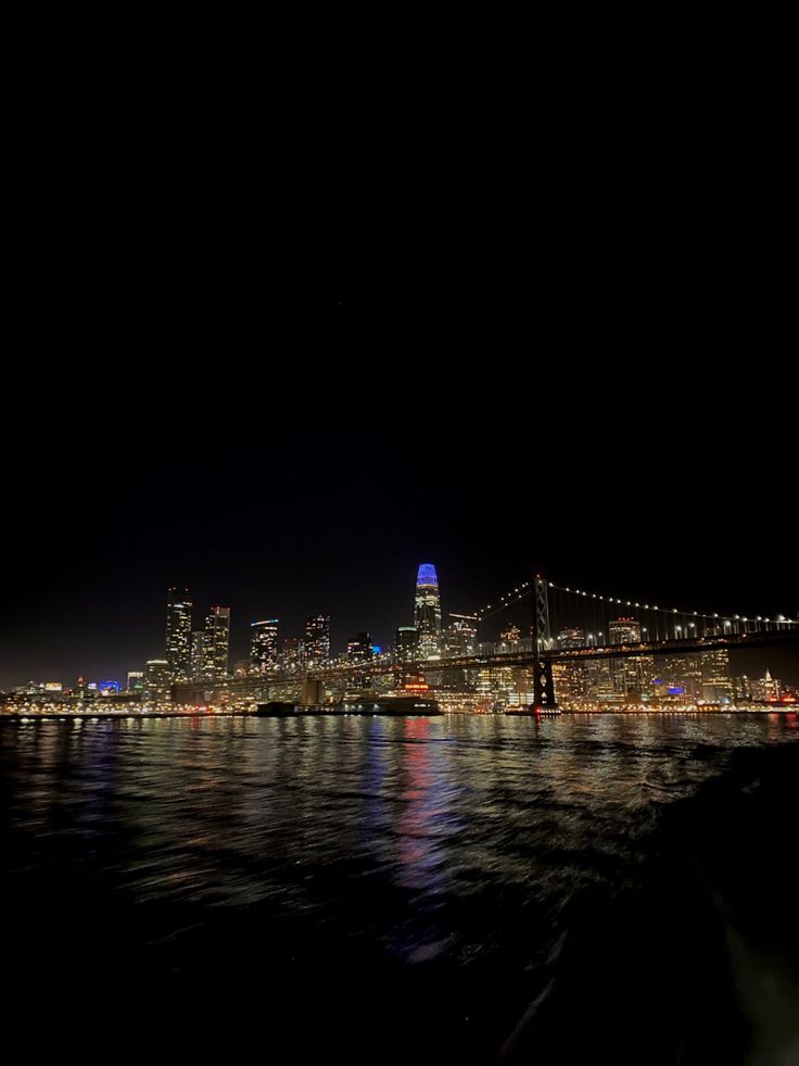 the city skyline is lit up at night as seen from across the water with lights reflecting in the water